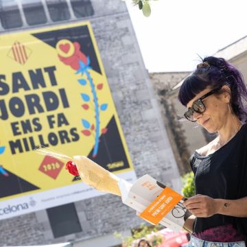 Una dona llegint amb el cartell de Sant Jordi ens fa millors© Àngel Bravo