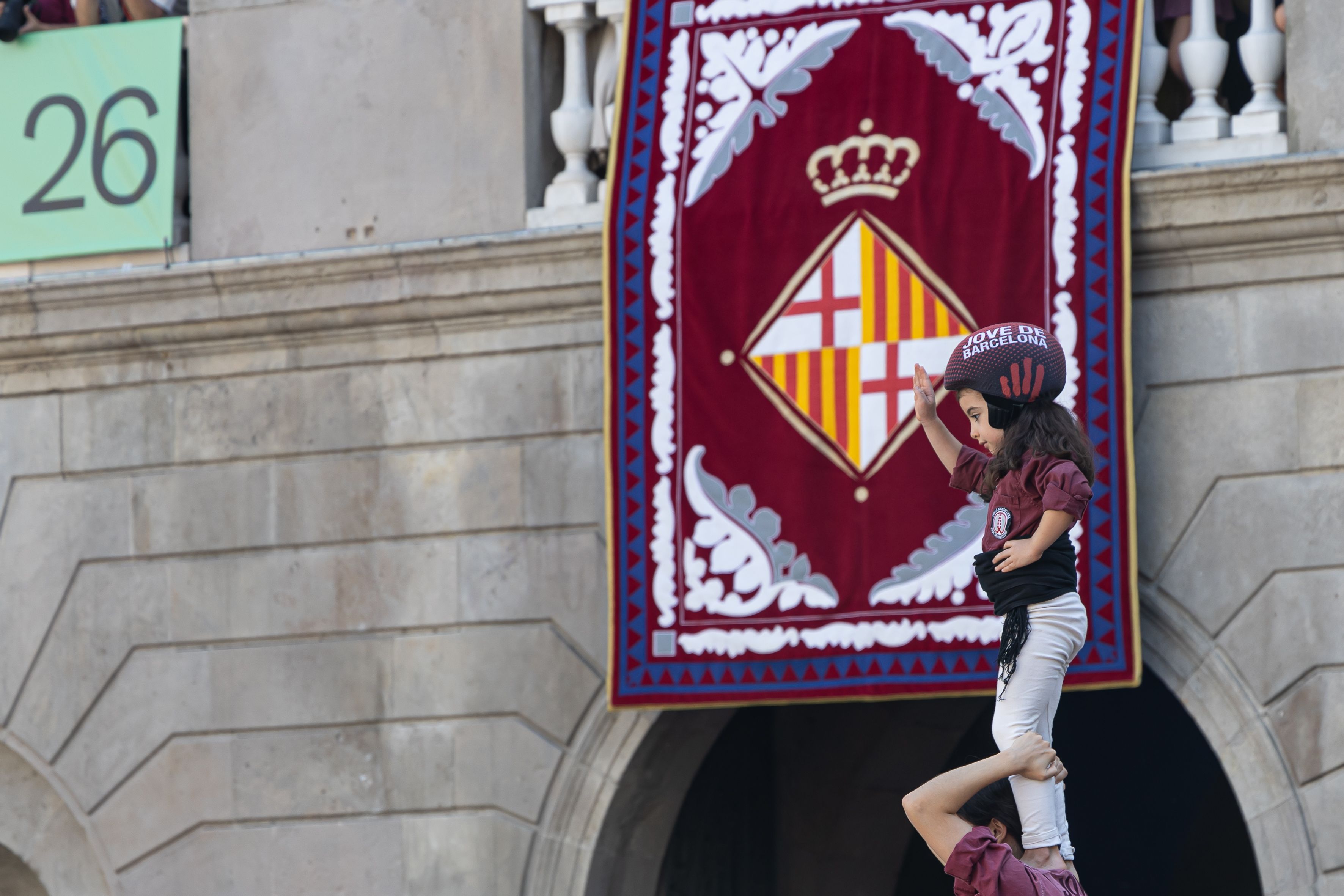 El anxaneta de la Colla Jove de Barcelona culmina el castell con el balcón del Ayuntamiento, engalanado con el escudo de la ciudad, como telón de fondo. © Àngel Bravo