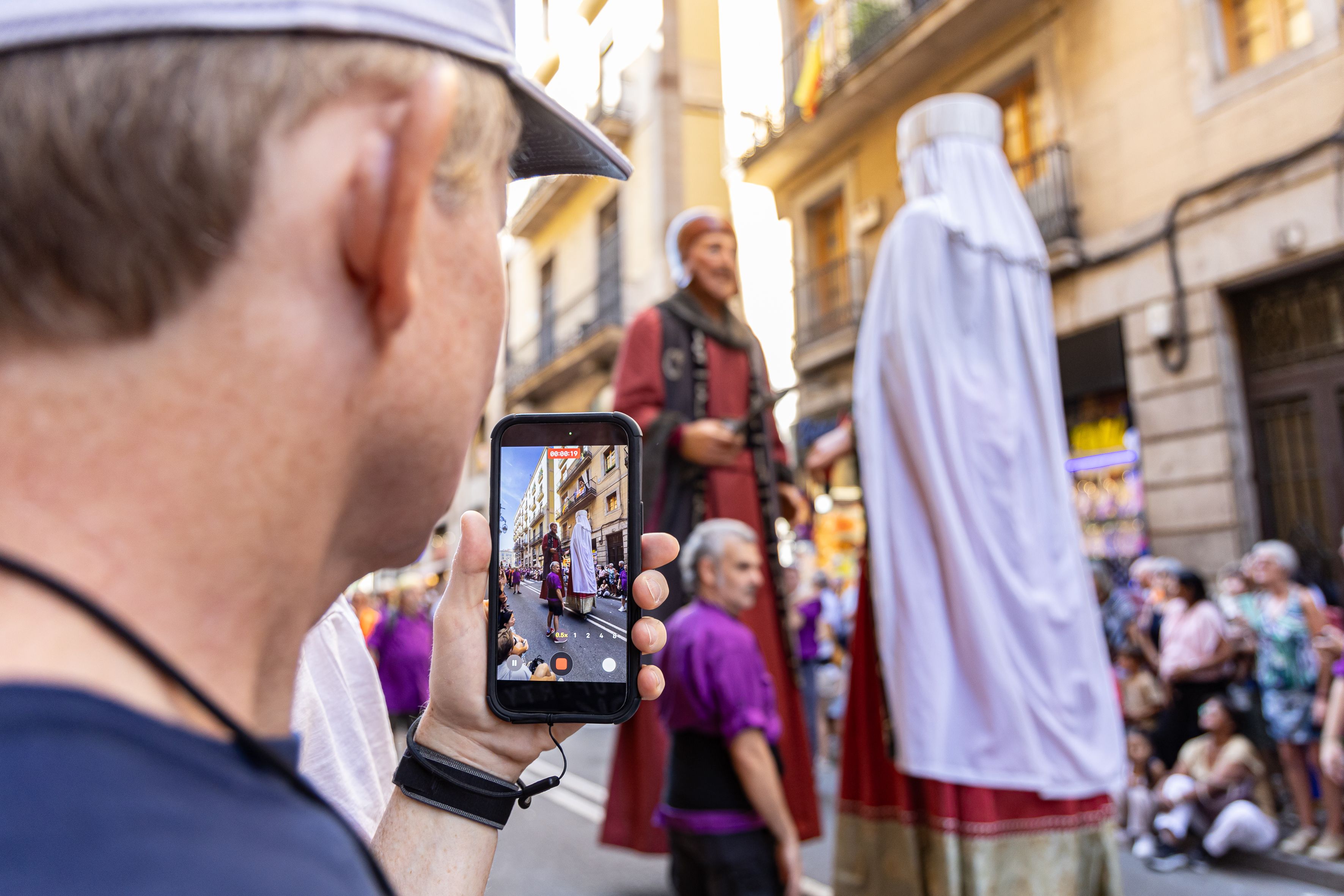 Con el móvil en la mano, un espectador graba el paso de los Nans i Gegants por las calles de Barcelona durante La Mercè. © Àngel Bravo