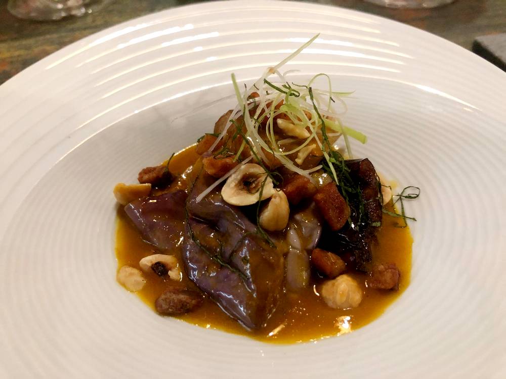 Berenjena thai con jugo de zanahoria en escabeche, vino Porto, cebolla y guanciale y avellanas.